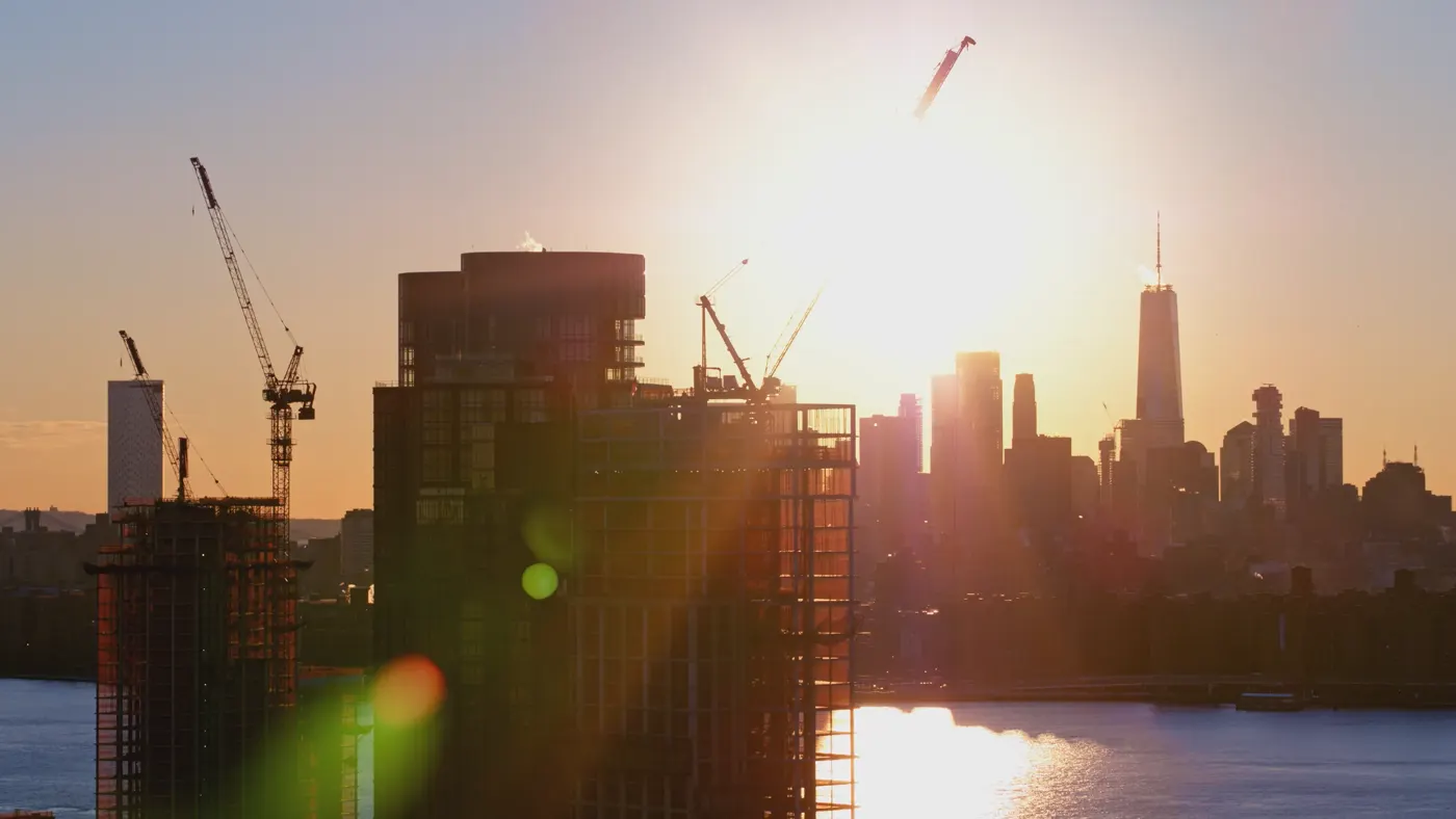 New residential towers' construction on the waterfront in Brooklyn, with the scenic view of Manhattan skyline, at sunset.