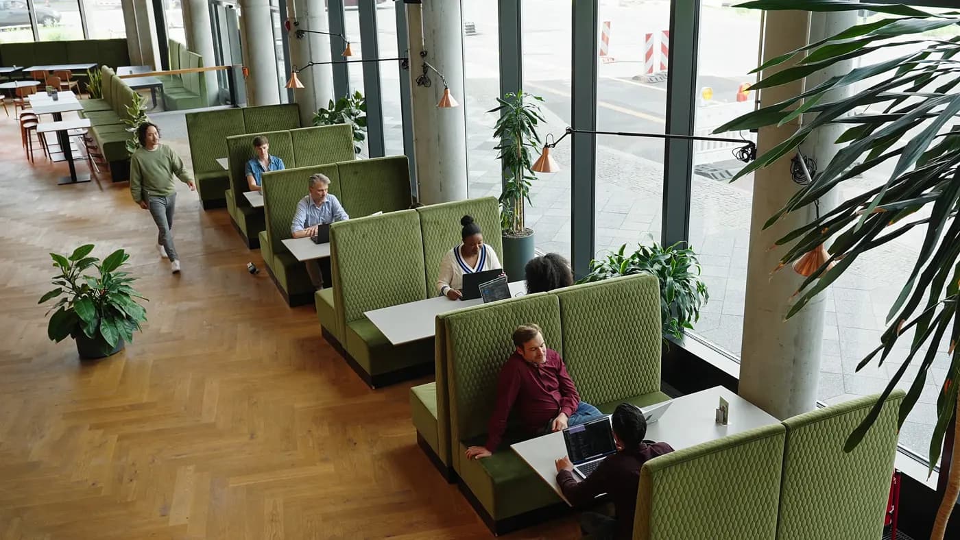 Modern office lounge with green booth seating, large windows and people working and meeting.