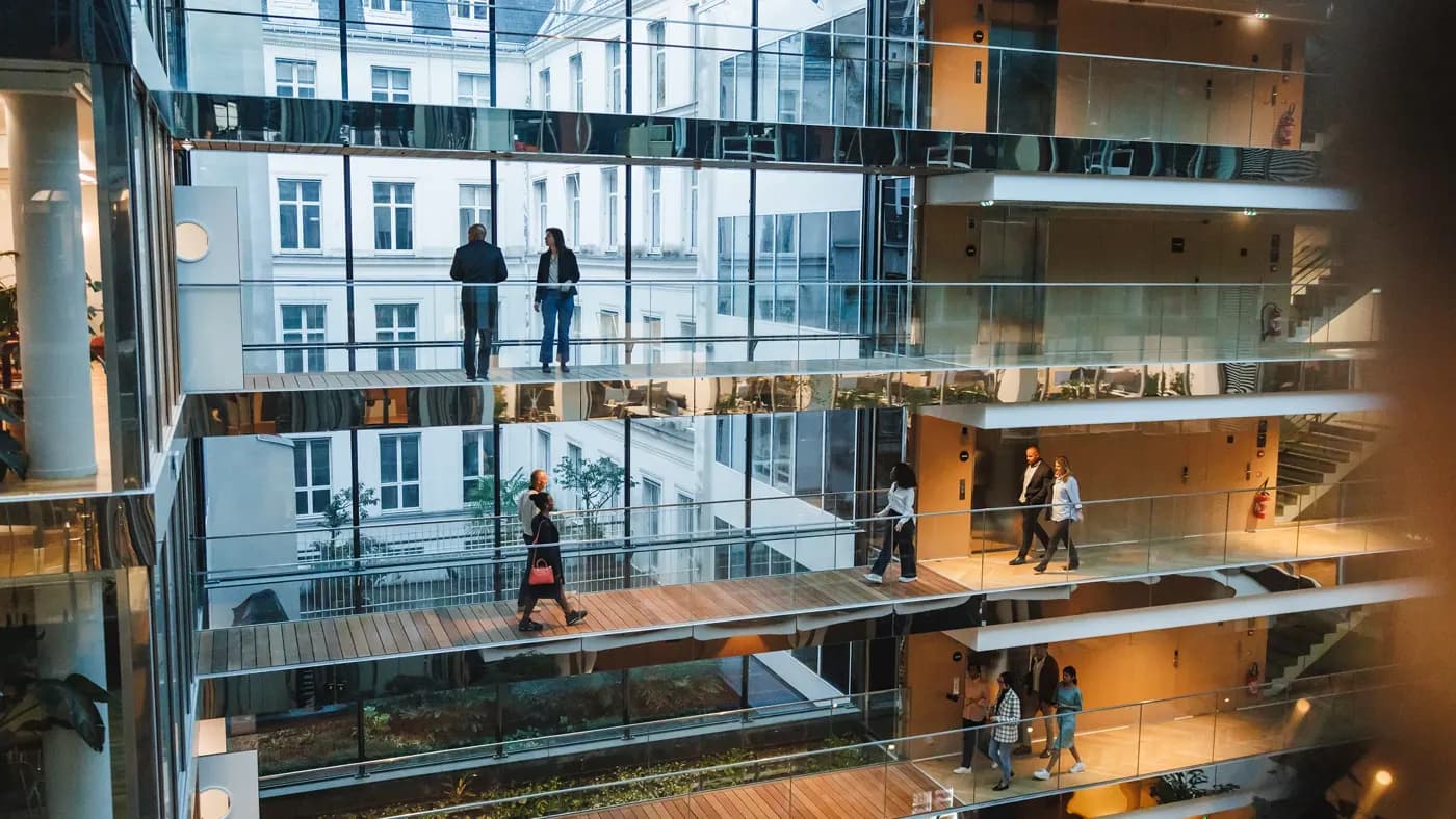 Open multi-storey office atrium with glass walkways and people walking between floors.