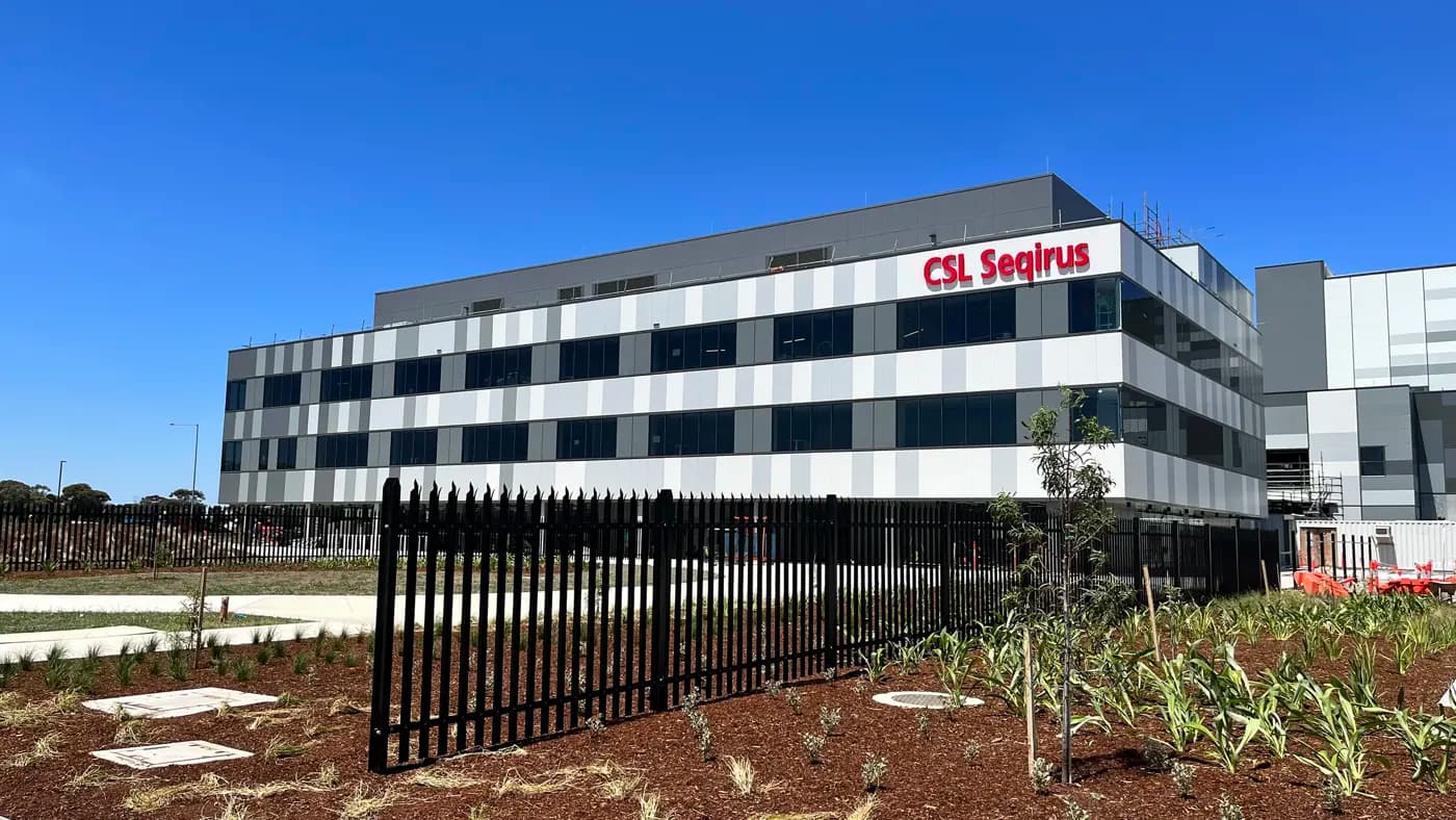 A CSL Seqirus vaccine facility, a multi-storey building set against a blue sky. 