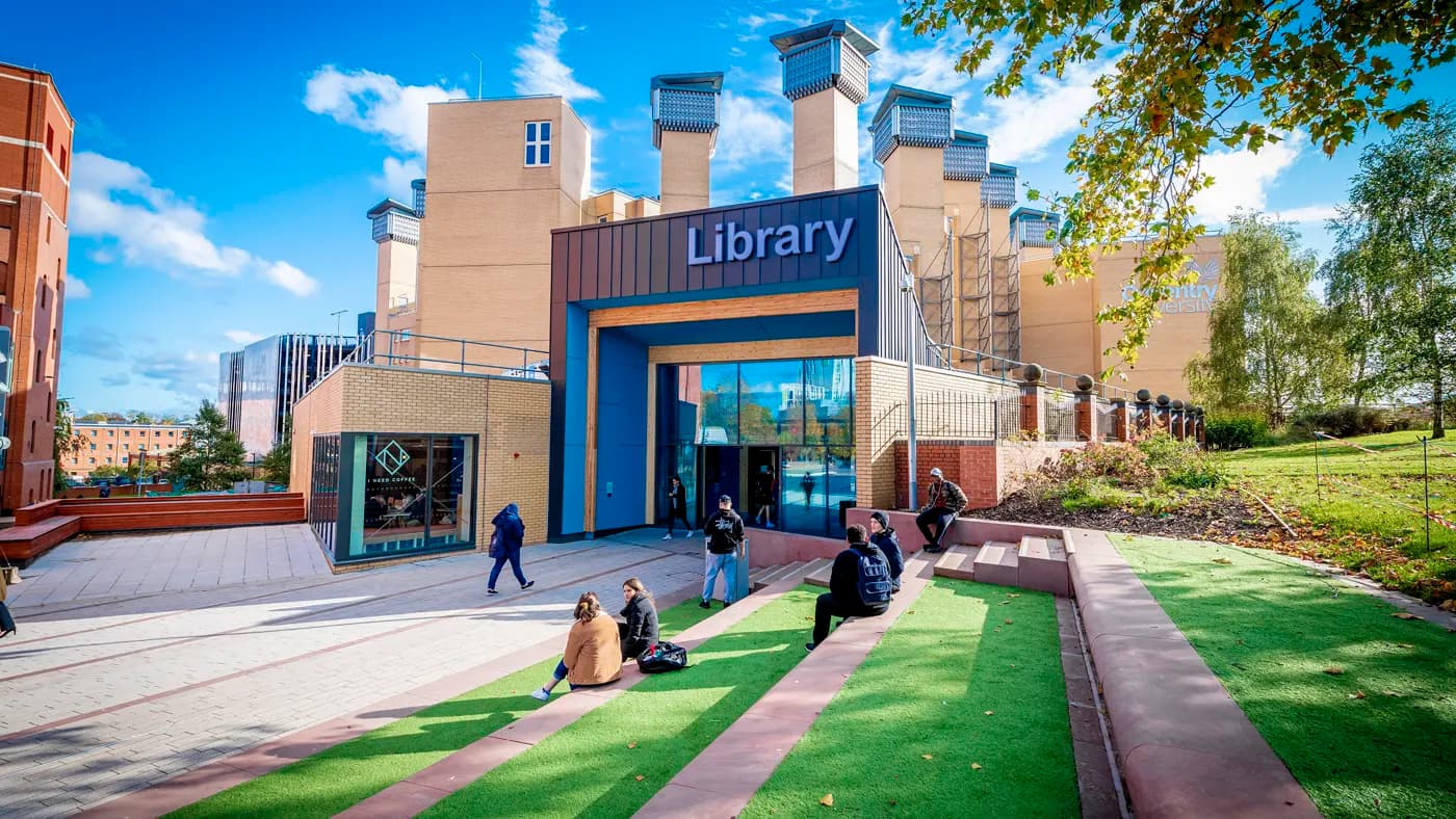Students sitting on a lawn and stairs outside a library building